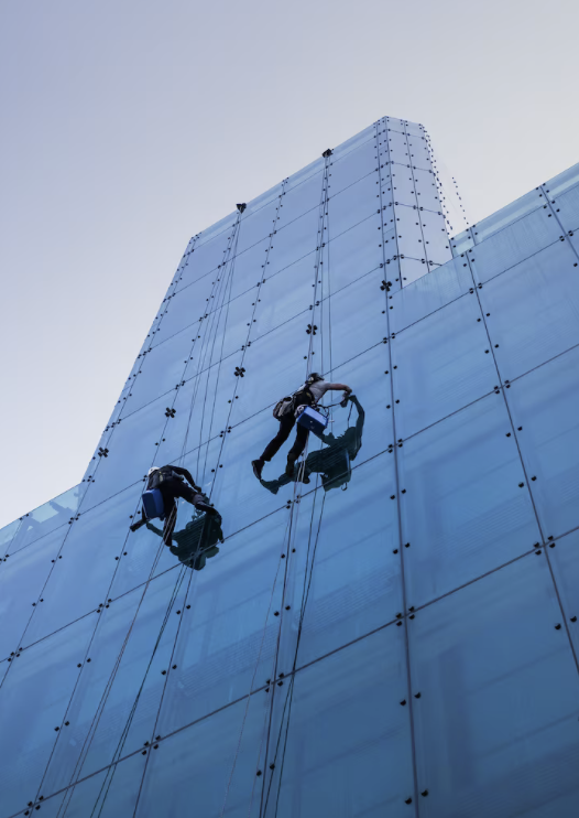 Fensterfassaden-Reinigung Zwei Fensterreiniger klettern an einer Glasfassade eines Hochhauses.