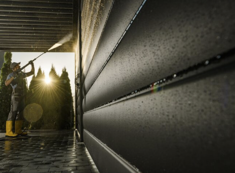 Fassaden-Reinigung Person im Gummistiefel reinigt eine Wand mit einem Hochdruckreiniger bei Sonnenuntergang.