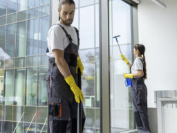 Zwei Reinigungskräfte putzen Fenster und Böden in einem modernen Bürogebäude.