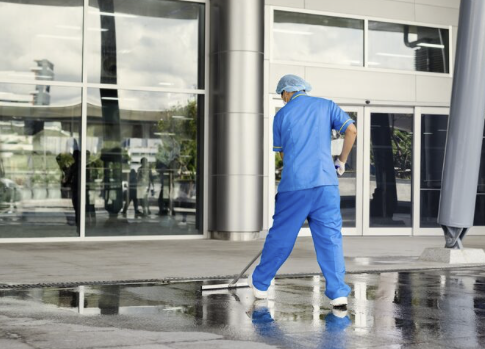 Pflaster-Reinigung Eine Reinigungskraft mit blauer Kleidung wischt den Boden eines modernen Gebäude.