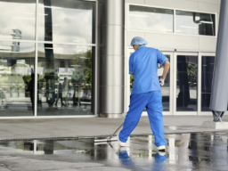 Ein Mann in blauer Arbeitskleidung reinigt den Boden eines modernen Gebäudes.
