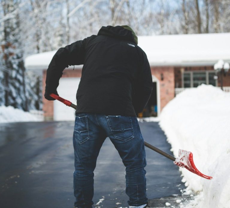 Hausmeister-Service Mitarbeiter schaufelt Schnee vor einem Haus in einer verschneiten Umgebung.