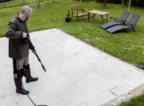 Terrassen-Reinigung Mann mit Hochdruckreiniger auf einer betonierten Tearrassen-Fläche im Garten.