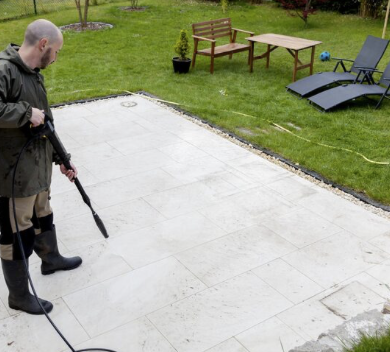 Tearrassen-Reinigung Mann reinigt mit dem Hochdruckreiniger eine Terrasse und die Bodenplatten.