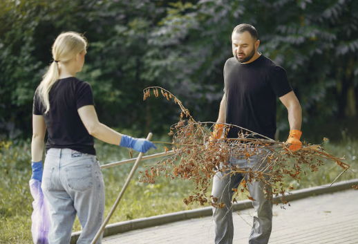 Grundstückspflege Zwei Personen sammeln gemeinsam Abfälle in einem Park, während sie Reinigungsutensilien verwenden.