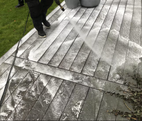 Holzboden-Reinigung Eine Person reinigt eine Holzterrasse mit einem Hochdruckreiniger und Seifenwasser.